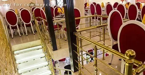 سالن غذاخوری مجلل رستوران ایرانی دهکده؛ دکوراسیون داخلی چشم‌نواز با چیدمان میز و صندلی‌های شیک قرمز و راه پله زیبای طلایی.