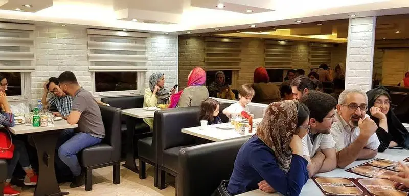 تصویری پویا از مشتریان در فست فود خانه کوچک در حال صرف غذا، گفتگو و لذت بردن از محیط گرم و خانوادگی رستوران.