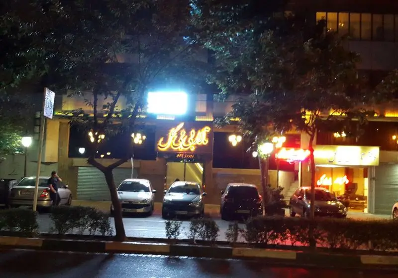 نمای بیرونی رستوران بی بی گل در شب با تابلوهای نورانی و چند خودروی پارک شده در خیابان، فضایی دلنشین و دعوت کننده برای شام.