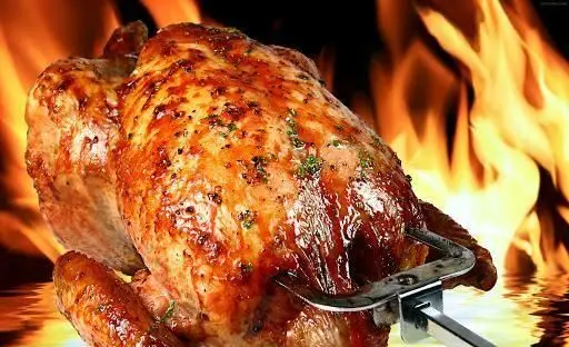 مرغ بریان طلایی و لذیذ، در حال چرخیدن روی شعله‌های آتش، آماده سرو در فست فود کره با بهترین کیفیت و طعم بی‌نظیر.