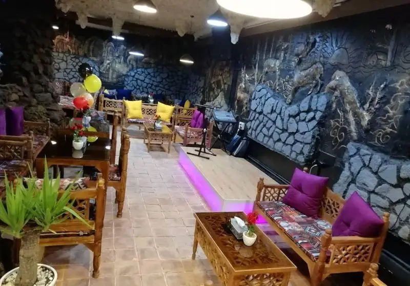 فضای داخلی دلنشین سفره خانه سنتی ماندگار با دیوارهای سنگی، مبلمان چوبی و طرح‌های سنتی، مناسب برای دورهمی و موسیقی زنده.