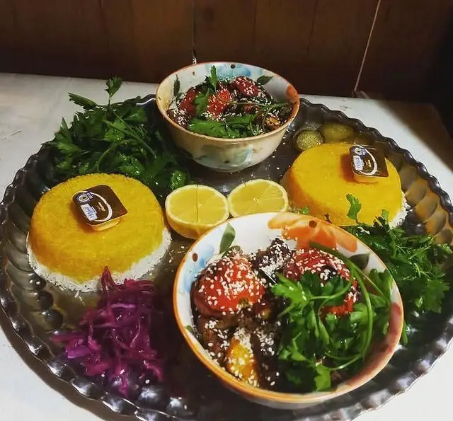 سفره آرایی دلنشین از غذاهای سنتی ایرانی: ته چین زعفرانی، خورش‌های مخصوص و سبزیجات تازه در سفره خانه سنتی ماندگار.