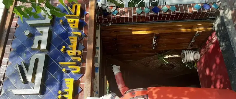 سفره خانه سنتی ماندگار: تابلو و ورودی با طراحی سنتی و اصیل ایرانی، حروف طلایی برجسته بر کاشی آبی، محیطی دلنشین