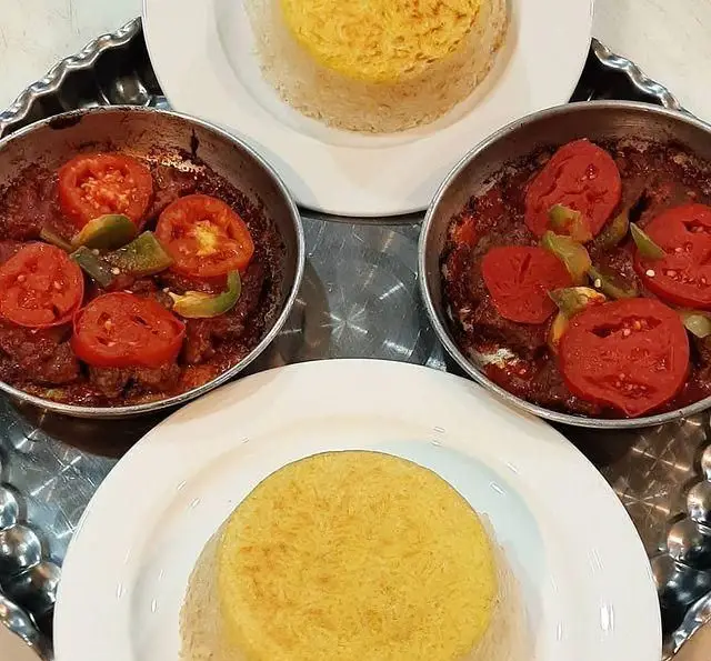 دو پرس غذای سنتی و خوشمزه ایرانی از سفره خانه ماندگار شامل کوفته یا خورش با گوجه و فلفل، در کنار برنج زعفرانی معطر.