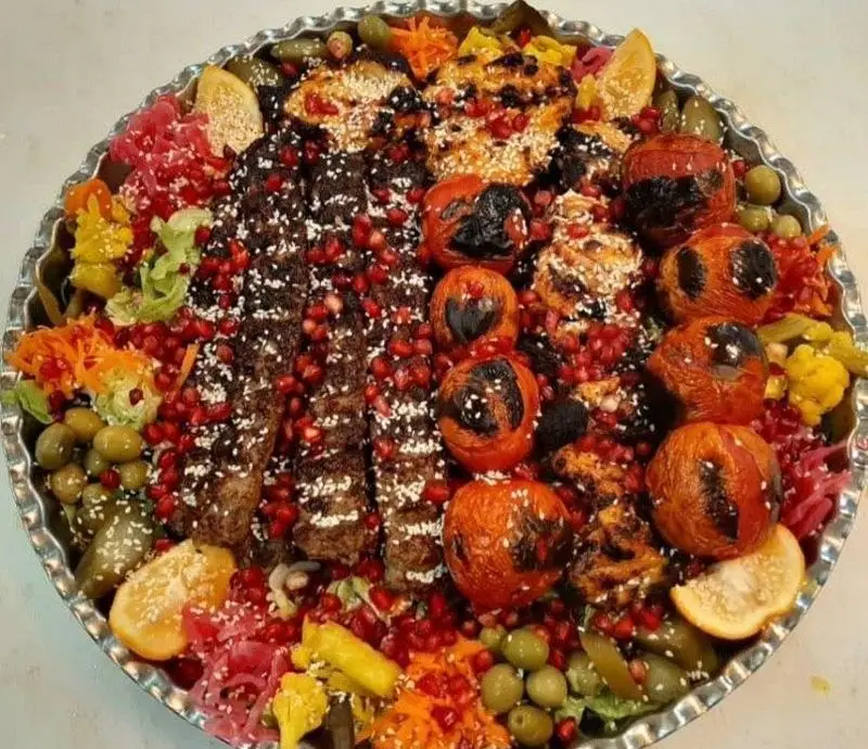 کباب کوبیده و جوجه کباب لذیذ با گوجه کبابی، تزئین شده با دانه انار، زیتون و انواع ترشیجات در سفره خانه سنتی ماندگار.