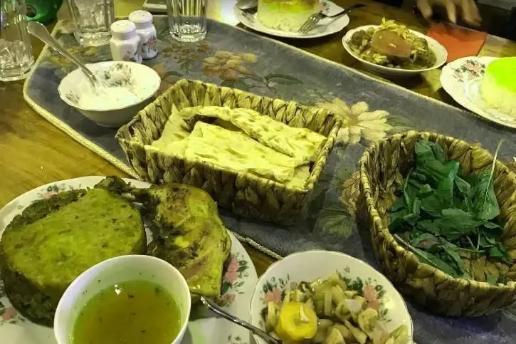 میز شلوغ و دلپذیر در رستوران ایرانی خونه با انواع غذاهای سنتی: قرمه‌سبزی، کوکو سبزی، مرغ، نان تازه و سبزی خوردن. تجربه اصیل ایرانی.