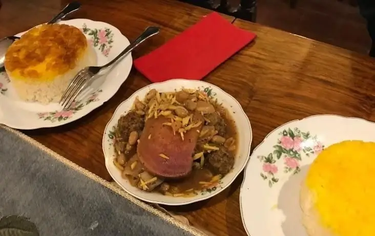 یک میز پر از غذای سنتی ایرانی از جمله آبگوشت دیزی یا کوفته و پلو زعفرانی با ته دیگ طلایی در رستوران ایرانی خونه