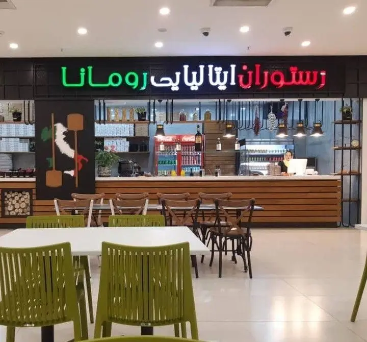 تصویری از فضای داخلی فودکورت رومانا، یک رستوران ایتالیایی شیک با دکوراسیون مدرن، میز و صندلی‌های سبز و سفید و پیشخوان چوبی.