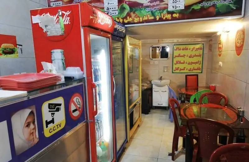 نمای داخلی فست فود پیتزا ساندویچ علی بابا با کانتر، یخچال نوشیدنی‌ها، منوی غذایی و میز و صندلی‌های مشتریان.