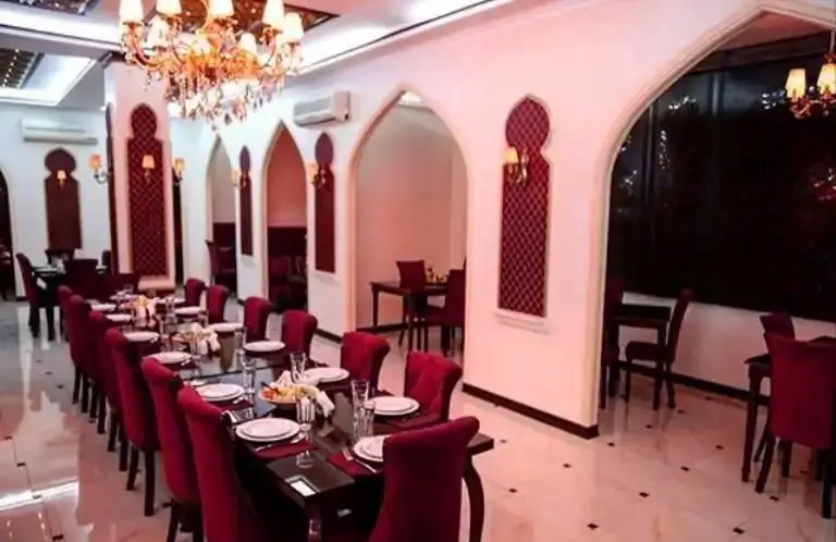 فضای داخلی لوکس کافی شاپ موروکو با میز بلند غذاخوری، صندلی‌های مخملی قرمز و دکوراسیون شیک عربی با طاق‌های زیبا و لوستر بزرگ.