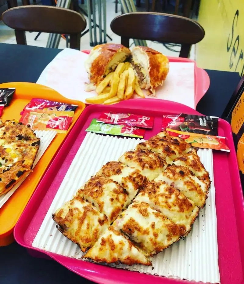 میزی پر از غذای فست فود در پیتزا هات شهرک غرب: ساندویچ غول‌پیکر، سیب‌زمینی، پیتزا مستطیلی پر پنیر و سس‌های متنوع.