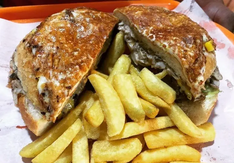 تصویری از ساندویچ فست فود لذیذ پیتزا هات شهرک غرب، حاوی پنیر یا تخم مرغ سرخ شده و انبوهی از سیب زمینی‌های سرخ شده.