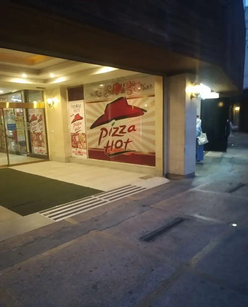 نمای بیرونی شعبه پیتزا هات شهرک غرب، با ورودی روشن و تابلوی بزرگ "Pizza Hot" برای جذب مشتریان فست فود.