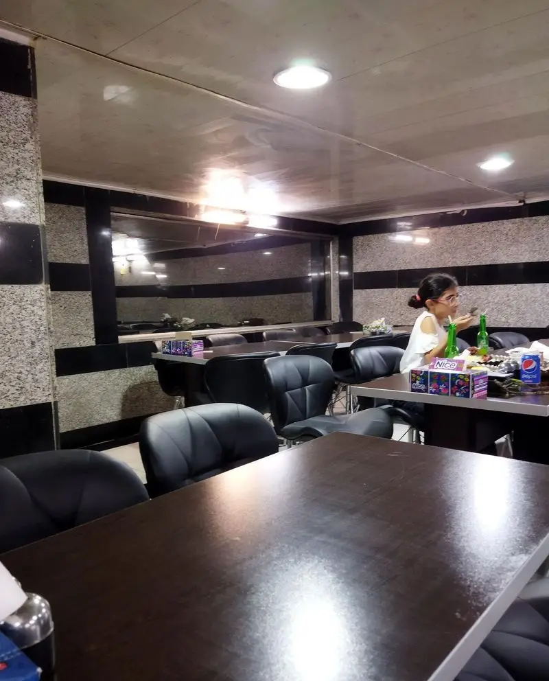 فضای داخلی رستوران حاتم با میز و صندلی‌های چرمی تیره، دیوارها با طرح گرانیت و آینه‌های بزرگ. مشتری در حال صرف نوشیدنی در این غذاخوری آرام.