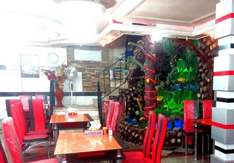 فضای داخلی رستوران قصر جگر بره طلایی با دکوراسیون جذاب شامل درخت نورانی، آبشار مصنوعی، میز و صندلی‌های قرمز و محیط دلنشین برای صرف جگر.