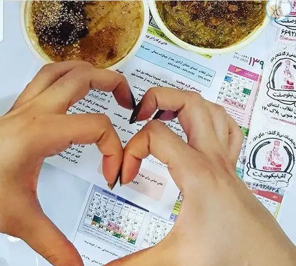 تصویر دست‌هایی به شکل قلب روی کاسه‌های آش و حلیم داغ و خوشمزه آش نیکوصفت، با اشاره به کیفیت عالی غذاهای سنتی ایرانی.