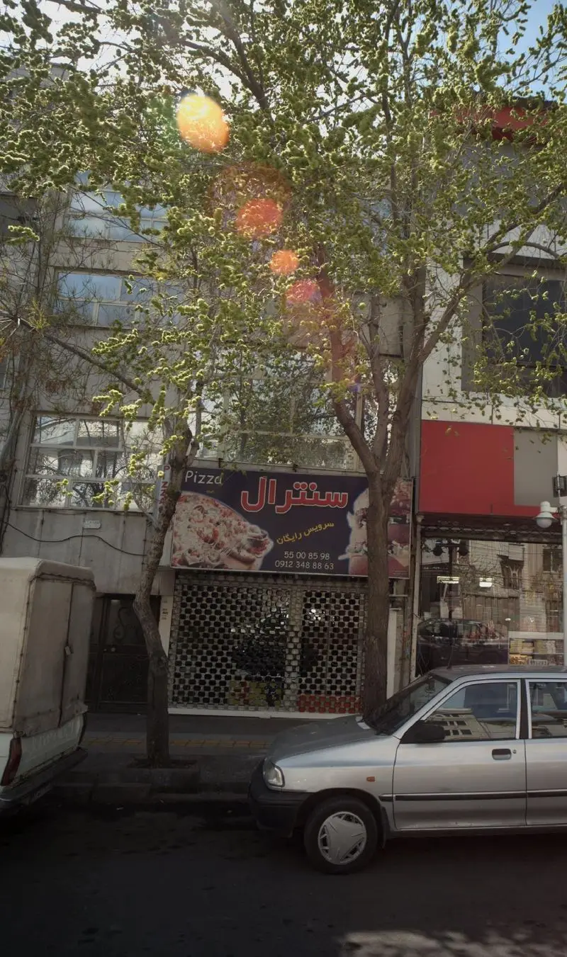 نمای بیرونی پیتزا سنترال با تابلوی روشن، تصویر پیتزا، شماره تماس و عبارت سرویس رایگان در یک روز آفتابی.