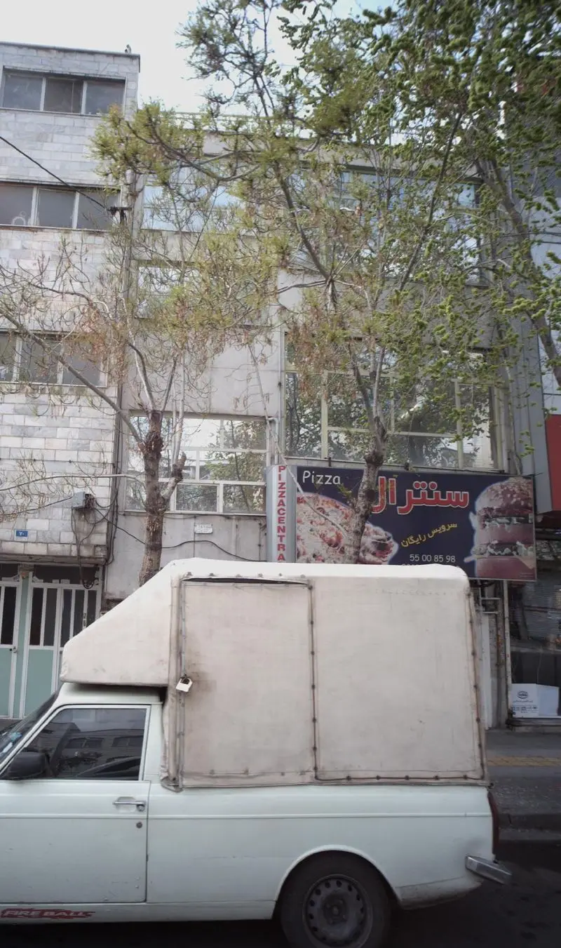 تصویر یک پیتزا فروشی سنترال با تابلوی بزرگ پیتزا و همبرگر در خیابان شلوغ شهر، آماده برای سفارش آنلاین و تحویل رایگان.