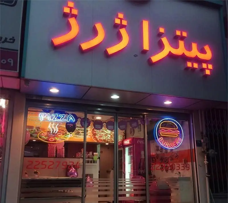 تصویری از سردر و ویترین فست فود پیتزا ژرژ، با تابلوهای نئون درخشان پیتزا و برگر در شب. بهترین پیتزا و برگر.