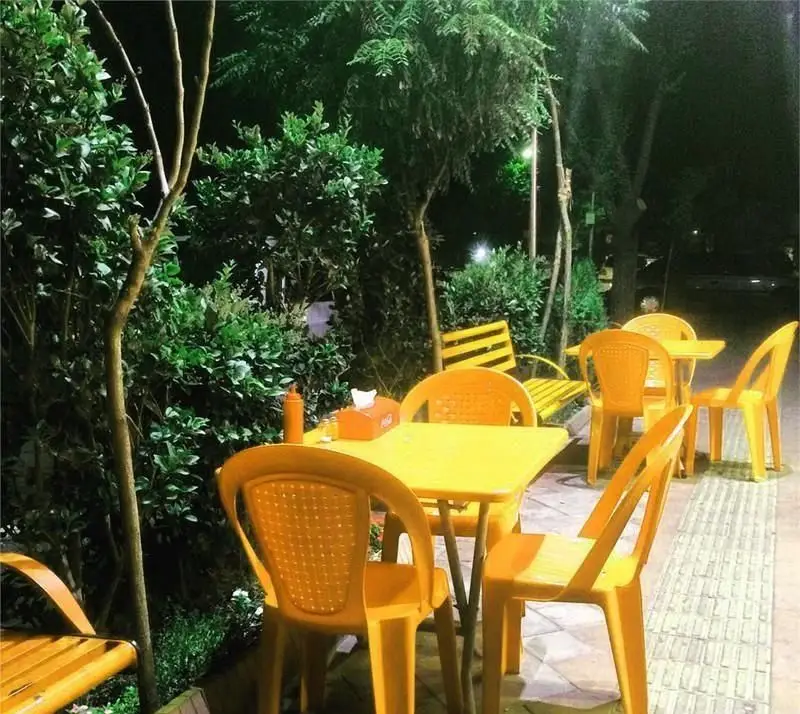 تصویری از محیط باز و شبانه کافه رستوران ژرژ، با چیدمان میز و صندلی‌های زرد کنار فضای سبز دلپذیر. تجربه‌ای آرامش‌بخش.