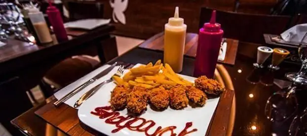 بشقاب مرغ سوخاری ترد و سیب زمینی سرخ کرده داغ در فست فود شاپرک، همراه با سس کچاپ که نام "شاپرک" روی آن نوشته شده است.