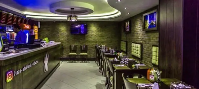 دکوراسیون داخلی مدرن و جذاب فست فود شاپرک تهران با دیوارهای آجری، تلویزیون و میز و صندلی‌های راحت برای مشتریان.