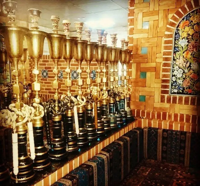 فضای داخلی دلنشین رستوران سنتی شب نشین با قلیان‌های آراسته و دیوارهای آجری مزین به کاشی‌کاری‌های زیبا.