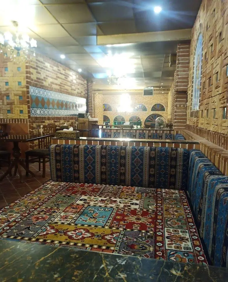 فضای داخلی دلنشین رستوران سنتی شب نشین با دکوراسیون ایرانی، دیوارهای آجری و فرش‌ها و نشیمن‌های سنتی جذاب.