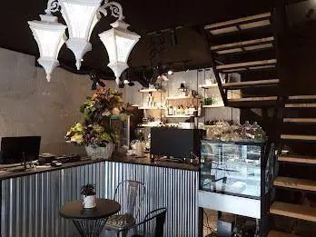 فضای داخلی کافه ایوان: دکوراسیون مدرن و دنج با پیشخوان فلزی راه‌راه، لوسترهای سفید، میز کوچک و پله‌های چوبی.