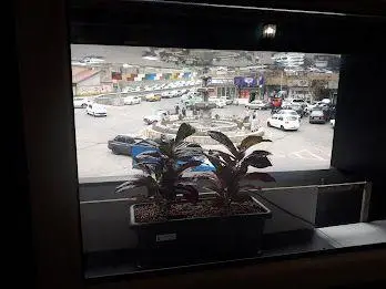 تصویری از داخل کافه ایوان با منظره پنجره رو به میدان اصلی شهر، شامل فواره و ترافیک خودروها، فضایی آرام و دلپذیر برای مشتریان کافه ایوان.