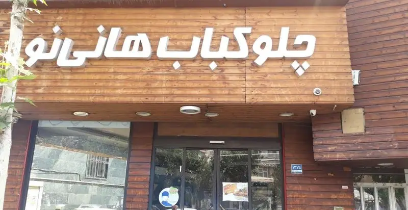 تصویری از نمای چوبی رستوران چلوکباب هانی نو با تابلوی سفید برجسته نام کسب و کار، ورودی و پنجره‌های شیشه‌ای