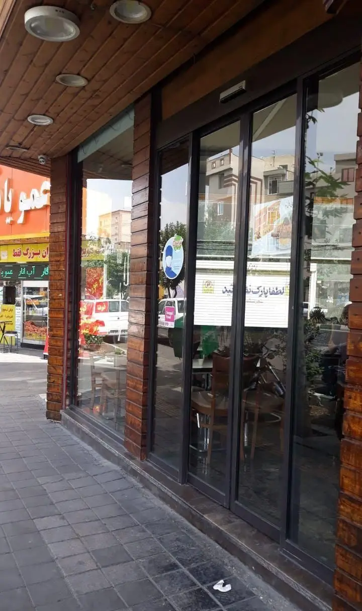 نمای بیرونی رستوران هانی نو با دکور چوبی و درب‌های شیشه‌ای مدرن. پیاده‌رو در جلوی ورودی، آماده پذیرایی از مشتریان با بهترین غذاها.