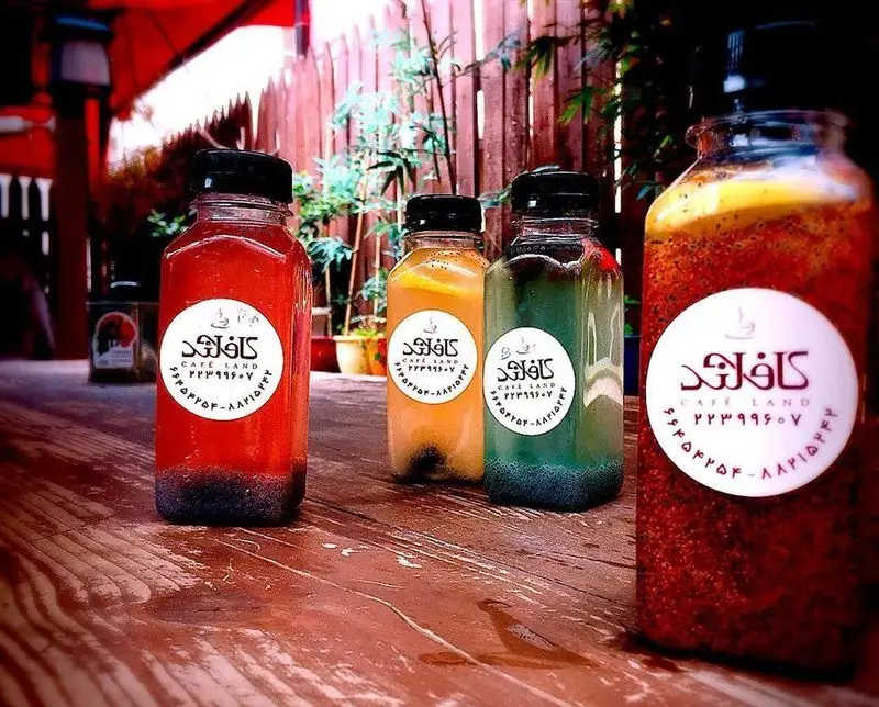 بطری‌های شیک نوشیدنی‌های میوه‌ای و خنک کافه لند با رنگ‌های جذاب روی میز چوبی. طعم‌های تازه و گوارای کافه لند برای هر سلیقه‌.