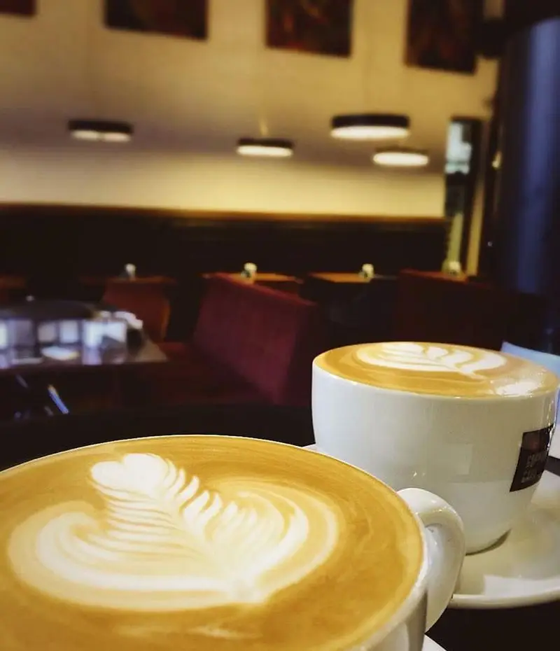 تصویری از دو فنجان قهوه لاته آرت بی‌نظیر در کافه لند، مکانی عالی برای تجربه طعم لذیذ و فضایی آرام و دلنشین.