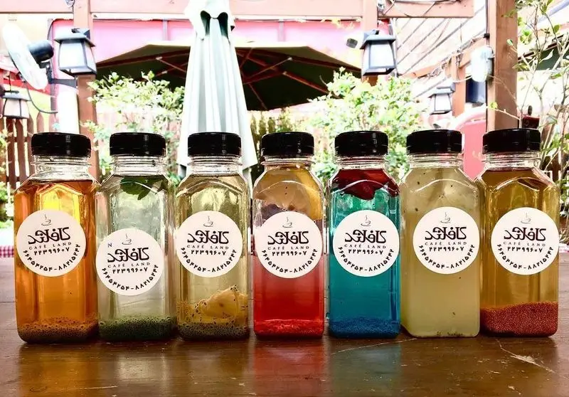 نوشیدنی‌های متنوع و رنگارنگ کافه لند در بطری‌های شیشه‌ای، با طعم‌های میوه‌ای و گیاهی، همراه با دانه‌های چیا، ایده‌آل برای تابستان.