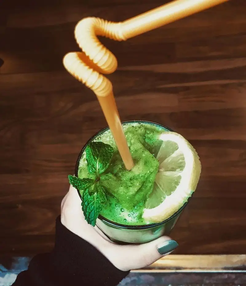 یک نوشیدنی اسموتی سبز تازه و سالم از کافه لند، با برگ‌های نعناع و برش لیمو، خنک و دلپذیر برای مشتریان کافه.