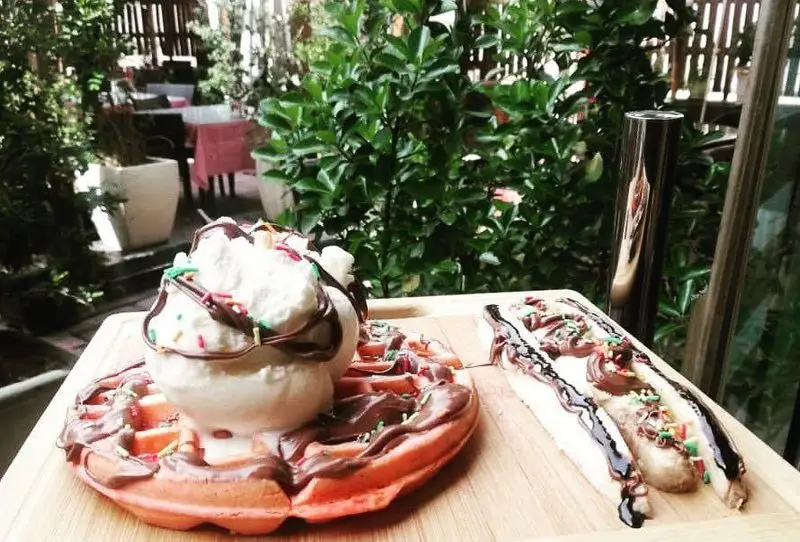 لذت دسر در کافه لند: وافل صورتی با بستنی، سس شکلات و اسپیرینکل، همراه موز با شکلات و اسپیرینکل در محیط دلنشین.