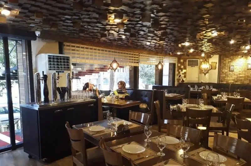 دکوراسیون داخلی رستوران پیتزا پاستا استیک با سقف مدرن، دیوارهای آجری، بار نوشیدنی و میزهای آماده برای پذیرایی مشتریان.