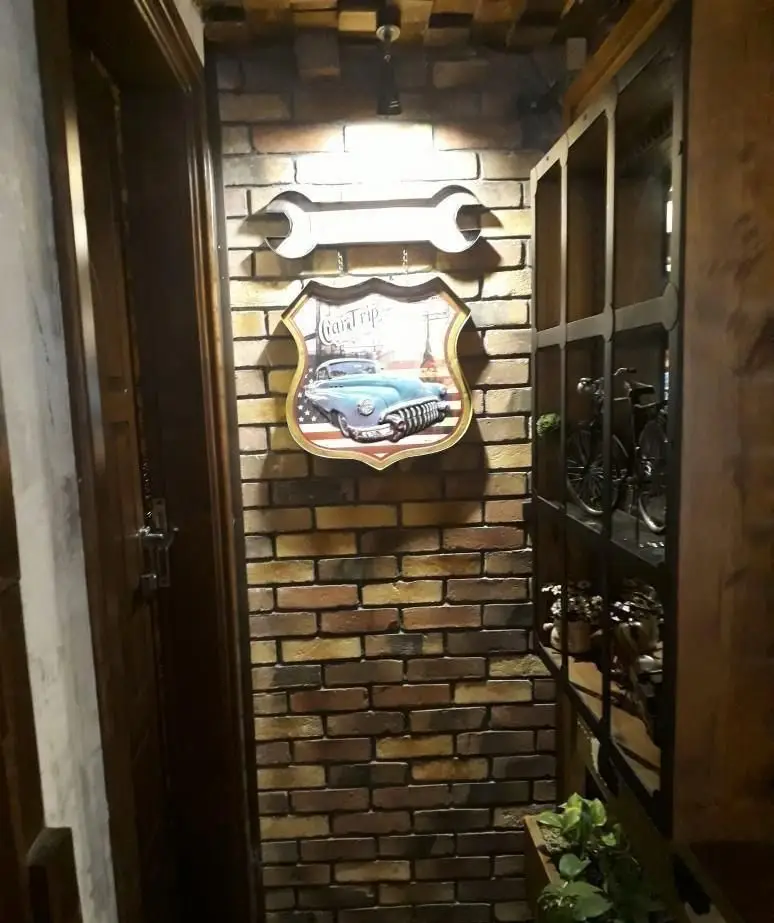 تصویری از دکوراسیون داخلی رستوران پیتزا پاستا استیک، شامل دیوار آجری، تابلوی ماشین کلاسیک و آچار، ایجاد فضایی جذاب و نوستالژیک برای مشتریان.