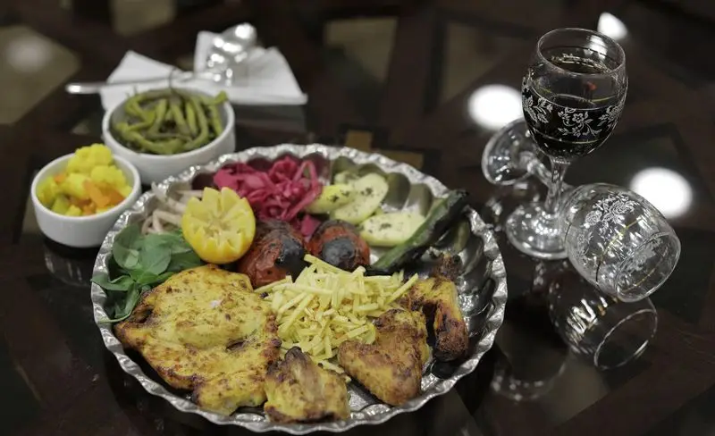 سینی غذای رستوران سنتی شهر آفتاب شامل جوجه کباب، سیب زمینی، گوجه و فلفل کبابی، سبزی، لیمو و ترشی با نوشیدنی در محیط دلنشین.