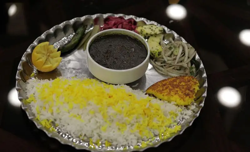 تصویر یک سینی غذای سنتی از رستوران شهر آفتاب: قورمه سبزی، پلو زعفرانی با ته دیگ طلایی، لیمو و دورچین‌های ایرانی تازه و اشتهاآور.