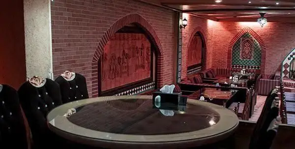نمایی از دکوراسیون داخلی رستوران فرنگی سنتی باران با دیوارهای آجری و طاق‌های قوسی شکل، میزهای چوبی و مبلمان سنتی با نورپردازی گرم