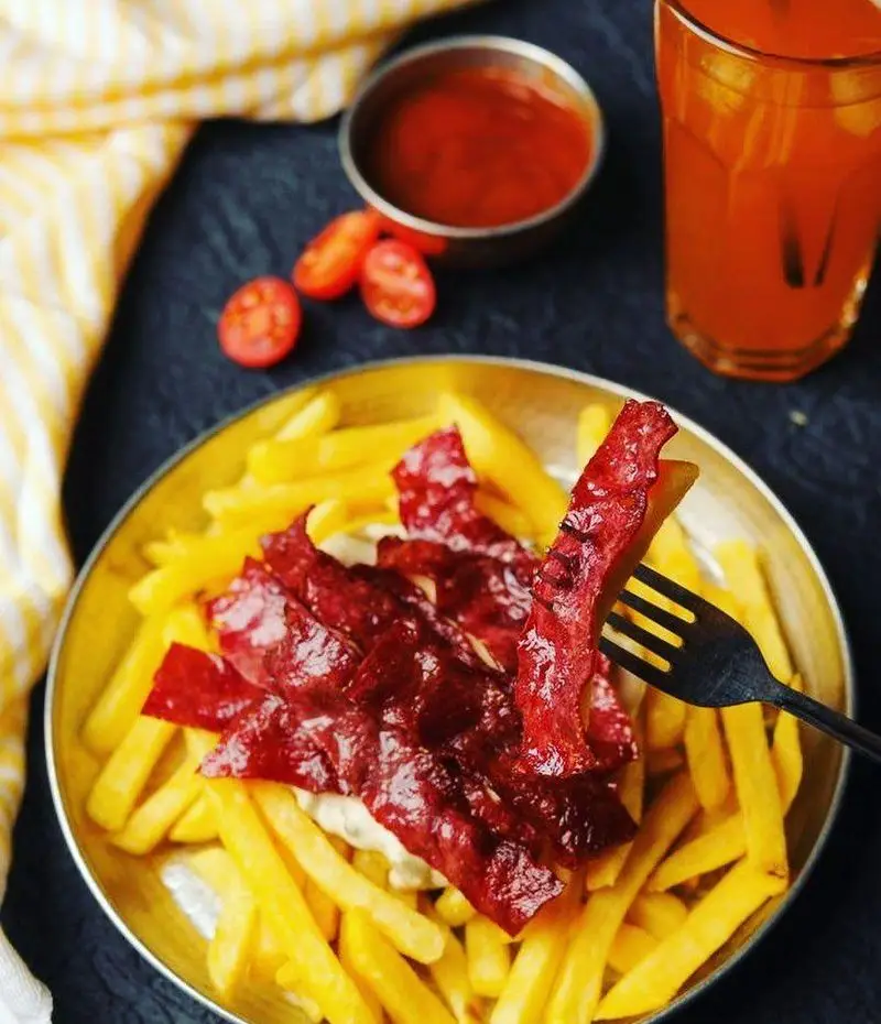 سیب زمینی سرخ کرده طلایی با تکه های گوشت قرمز و سس مخصوص، همراه با سس گوجه و نوشیدنی در رستوران پیاله.