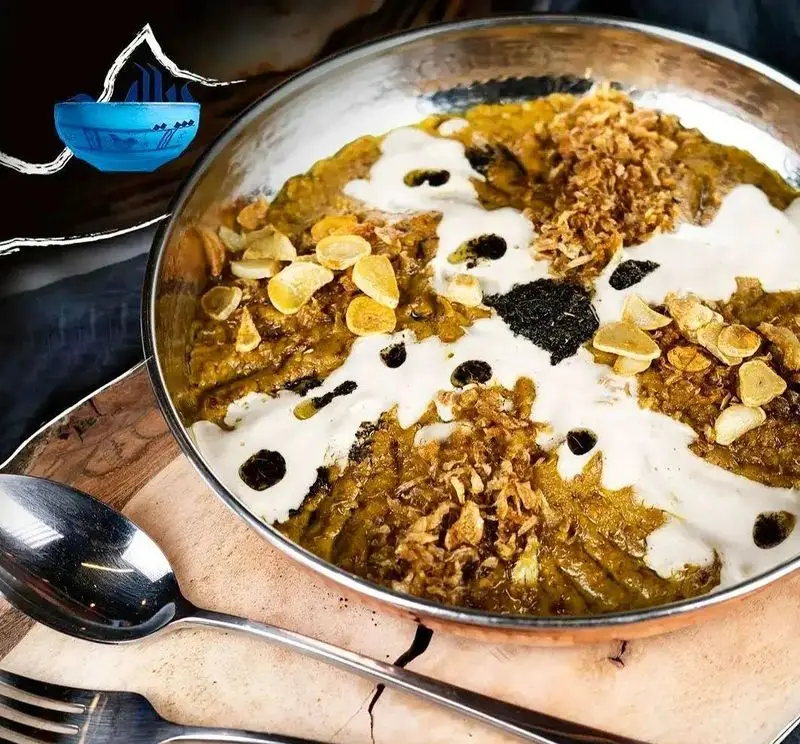 نمای نزدیک از یک کاسه غذای سنتی و لذیذ از رستوران پیاله، با تزئین کشک، سیر داغ، پیاز داغ و سبزی معطر، تجربه‌ای متفاوت از طعم.