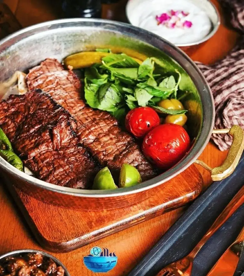 کباب گوشت آبدار رستوران پیاله در سینی مسی، همراه با گوجه کبابی، سبزیجات معطر، زیتون و چاشنی لیمو. طعم بی‌نظیر غذای اصیل ایرانی.