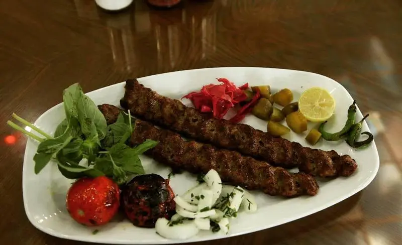 تصویری جذاب از چلوکباب کوبیده رستوران پیاله با مخلفات کامل شامل گوجه کبابی، سبزی، پیاز، ترشی و فلفل سبز. غذای اصیل ایرانی.