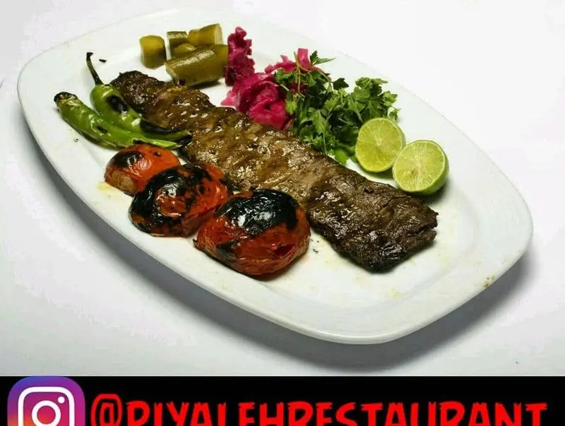 عکس کباب برگ خوشمزه و آبدار رستوران پیاله با چیدمانی زیبا شامل گوجه، فلفل، خیارشور، سبزیجات و لیمو. غذای ایرانی اصیل.