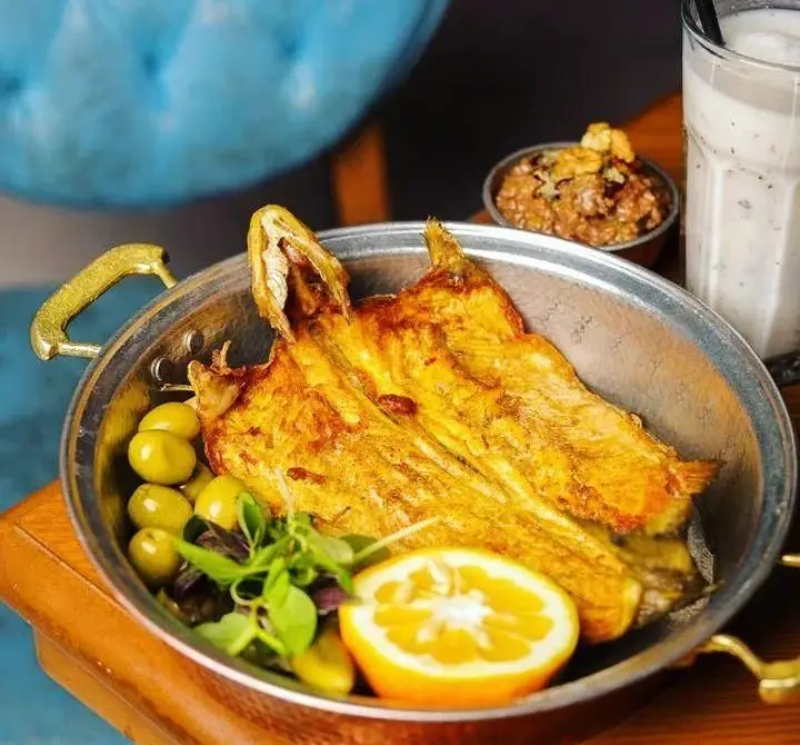 ماهی سرخ شده لذیذ با زیتون سبز، لیموترش تازه و سبزیجات معطر در رستوران پیاله. تجربه یک وعده غذایی دریایی اصیل و خوش‌طعم.