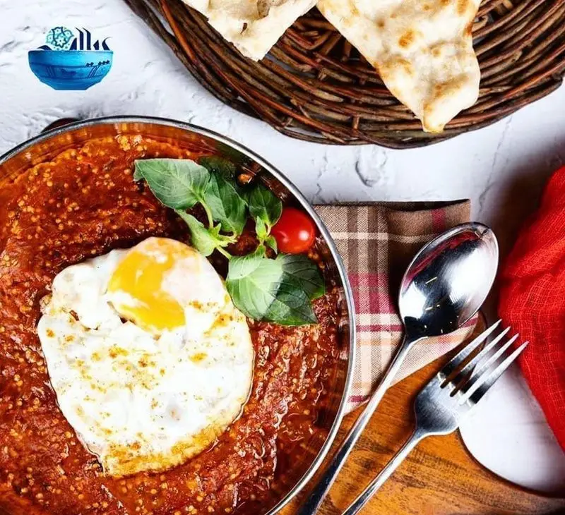 صبحانه لذیذ و دلنشین رستوران پیاله: املت با سس گوجه فرنگی تند، سبزیجات معطر تازه و نان سنگک گرم در سینی چوبی.