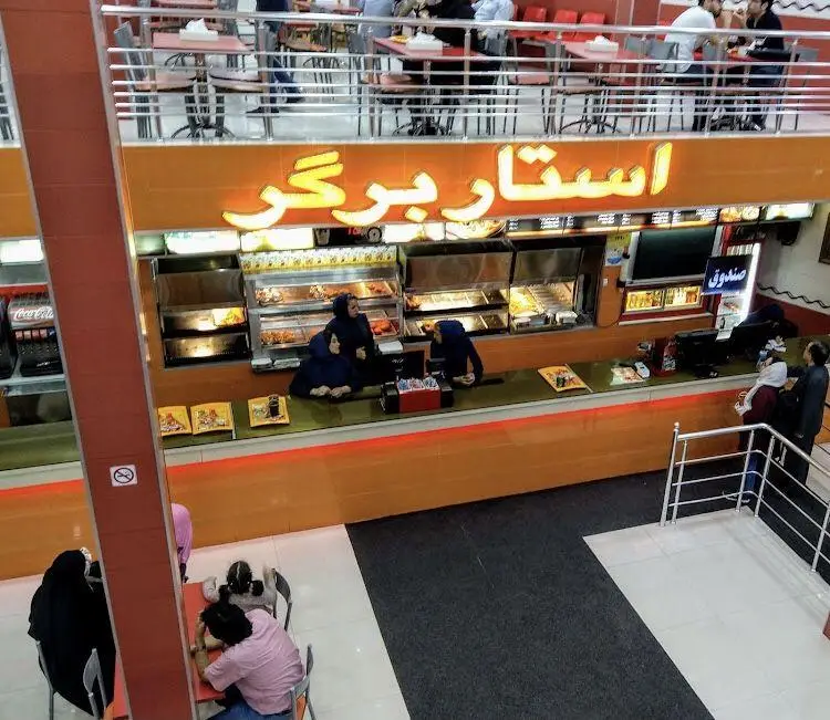 تصویر گسترده از فضای داخلی رستوران فست فود استار برگر شامل پیشخوان، پرسنل و مشتریان در حال غذا خوردن در دو طبقه.